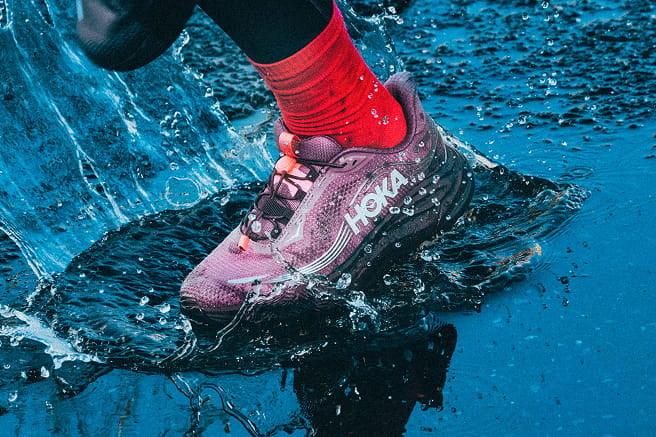 Gros plan d’une personne mettant les jambes dans l’eau en portant des chaussures HOKA.